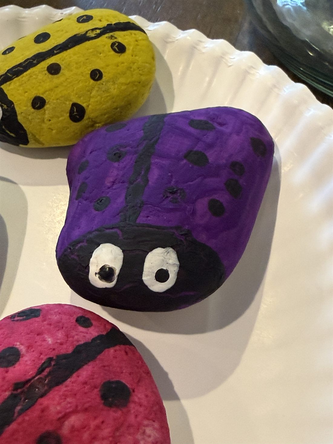 Close-up of a rock painted as a purple ladybug with hand-painted white eyes